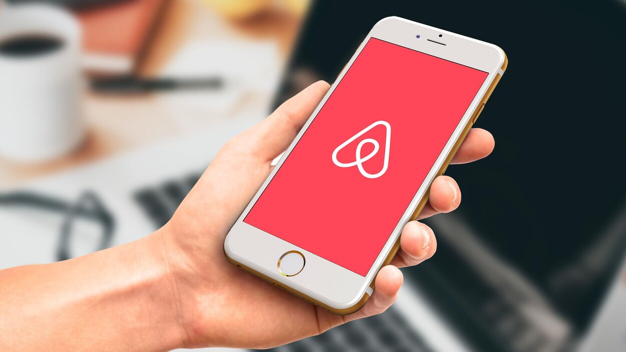 Une main tient un téléphone portable muni de l’application Airbnb.