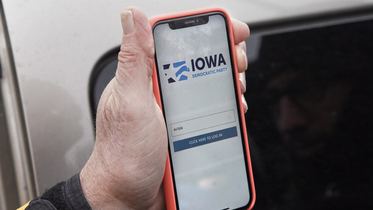 Un homme tient dans sa main son téléphone cellulaire; on y voit l'application Iowa Democratic Party.