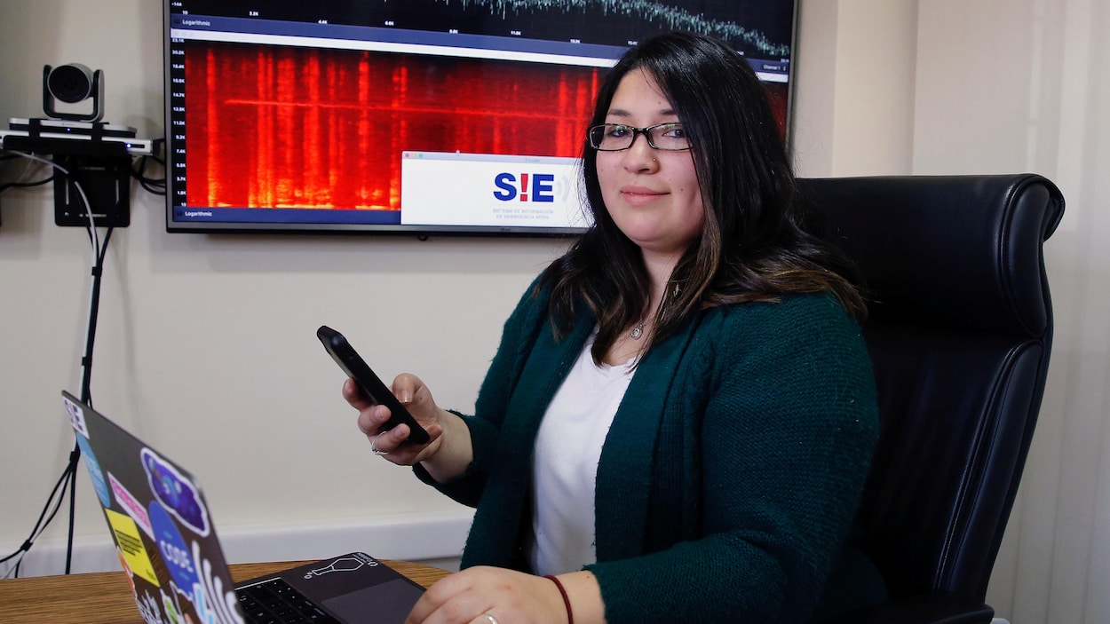Barbarita Lara pose devant son ordinateur et tient un téléphone intelligent à la main.