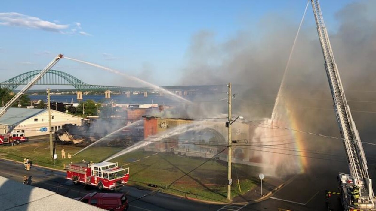 Une photo prise de haut de la municipalité de Miramichi au Nouveau-Brunswick. Des pompiers sont au prise avec une incendie au théâtre Vogue et un arc-en-ciel est créée par le contraste entre le temps chaud et l'eau projetée par les équipes.