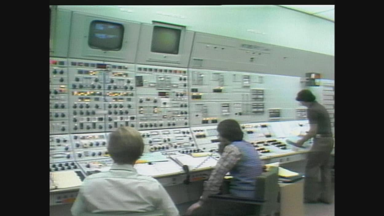 Trois hommes dans une centrale électrique. Devant eux, des écrans et des boutons. Trois hommes dans une centrale électrique. Devant eux, des écrans et des boutons.