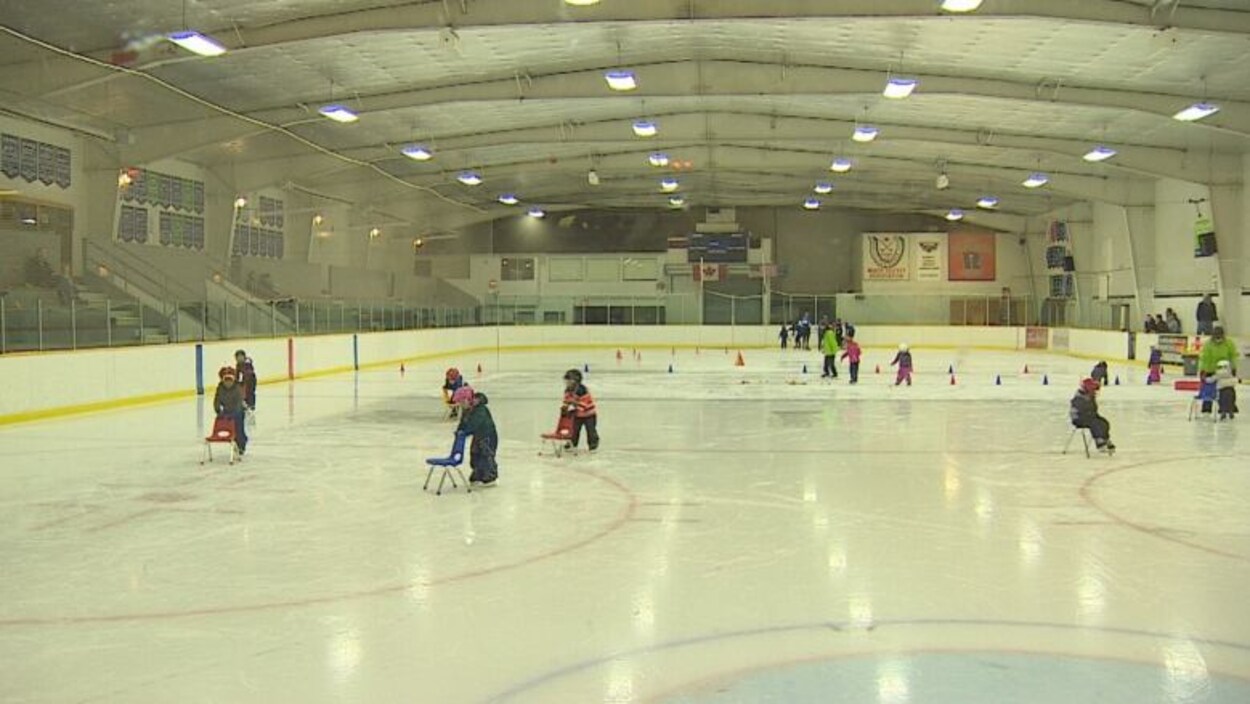 Des jeunes enfants patinent avec des chaises sur une patinoire.