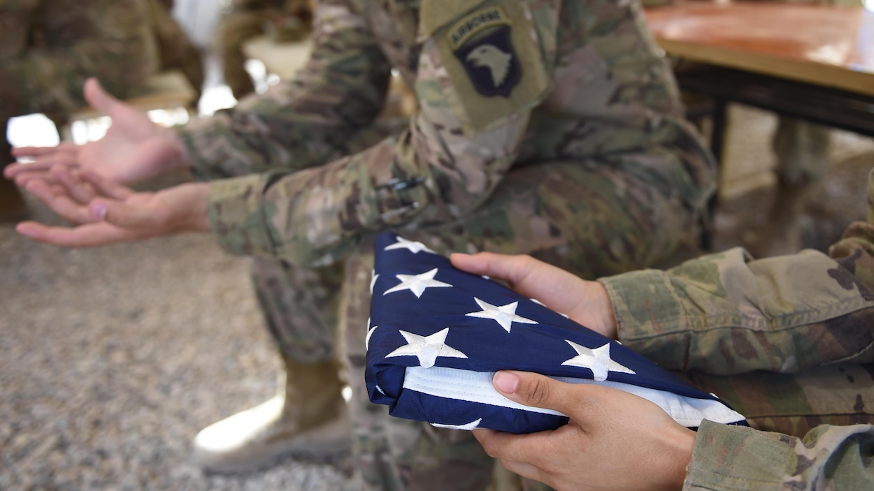 Un soldat tient un drapeau américain plié en forme de triangle