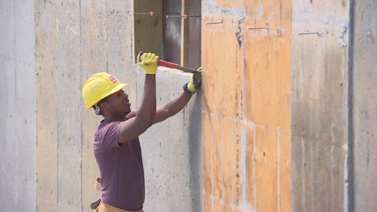 Un homme portant un casque de construction et des gants enlève le coffrage d'une fondation à l'aide d'un marteau. Un homme portant un casque de construction et des gants enlève le coffrage d'une fondation à l'aide d'un marteau.