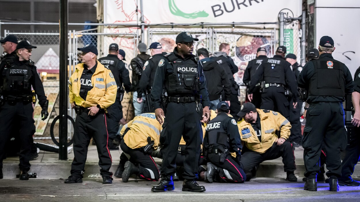 Photo d'une demi-douzaine de policiers qui entourent un suspect au sol, alors que d'autres agents passent les menottes à des jeunes hommes près d'une clôture.