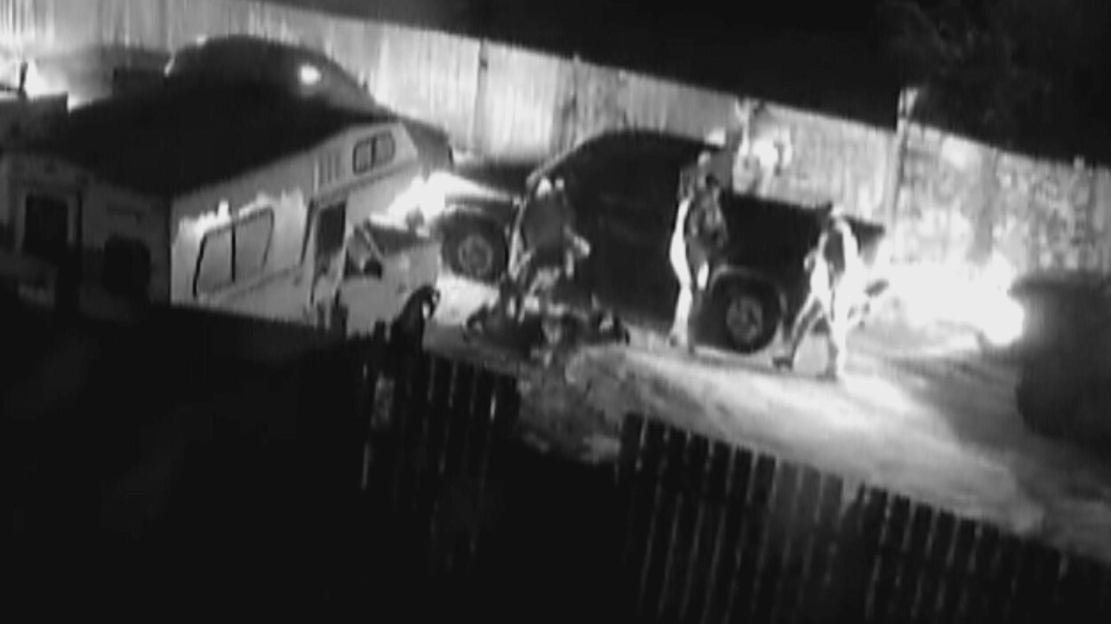Une image en noir et blanc tirée de la vidéo de surveillance montrant les policiers et les suspects autour d'une camionnette.