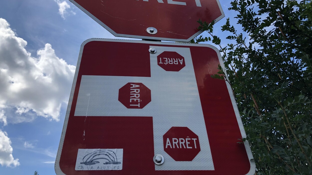 Un panneau d'arrêt où on distingue en bas l'autocollant d'arc-en-ciel.
