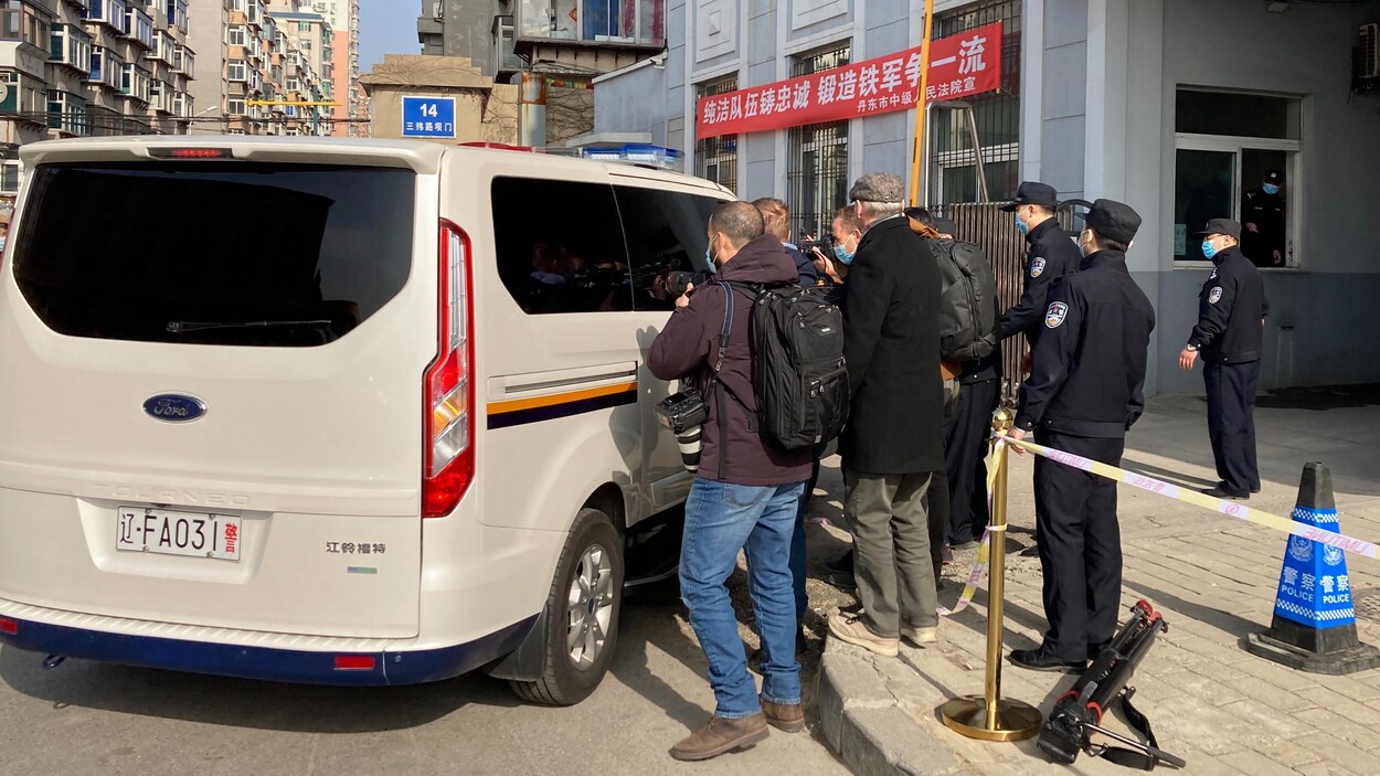 Plusieurs hommes se pressent autour d'un fourgon de la police, sous le regard de policiers chinois. 