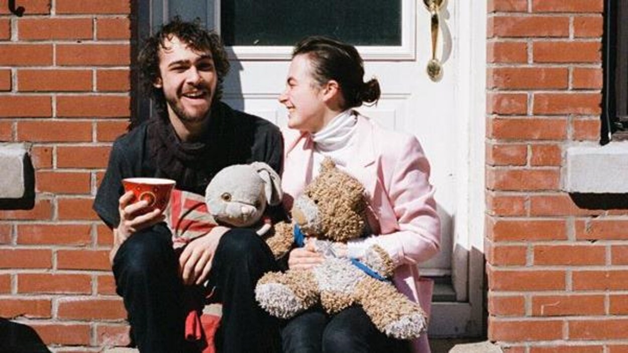 Un couple souriant est assis sur des marches devant leur maison.