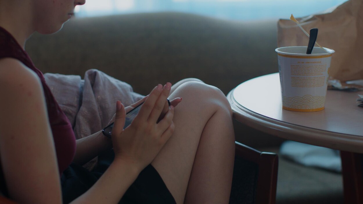 La jeune fille est assise et regarde son téléphone.