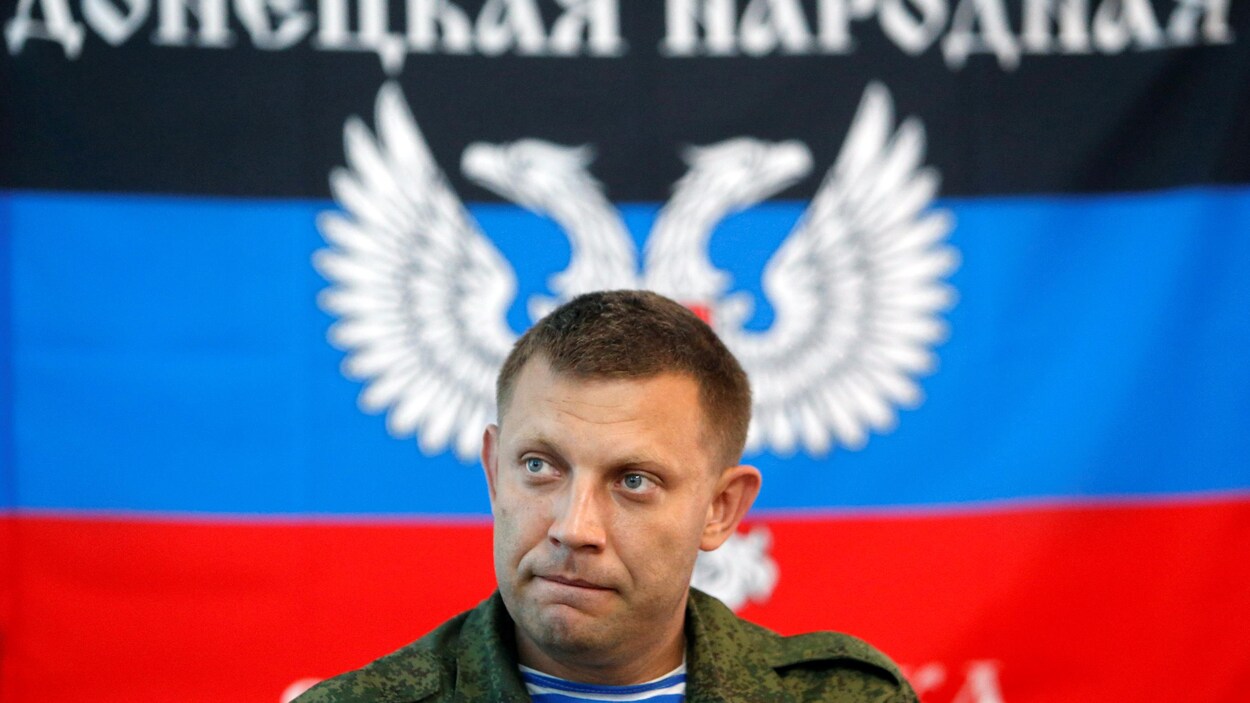 Alexandre Zakhartchenko, des épaules en montant, regard sérieux, en habit militaire, devant un drapeau de sa République autoproclamée.