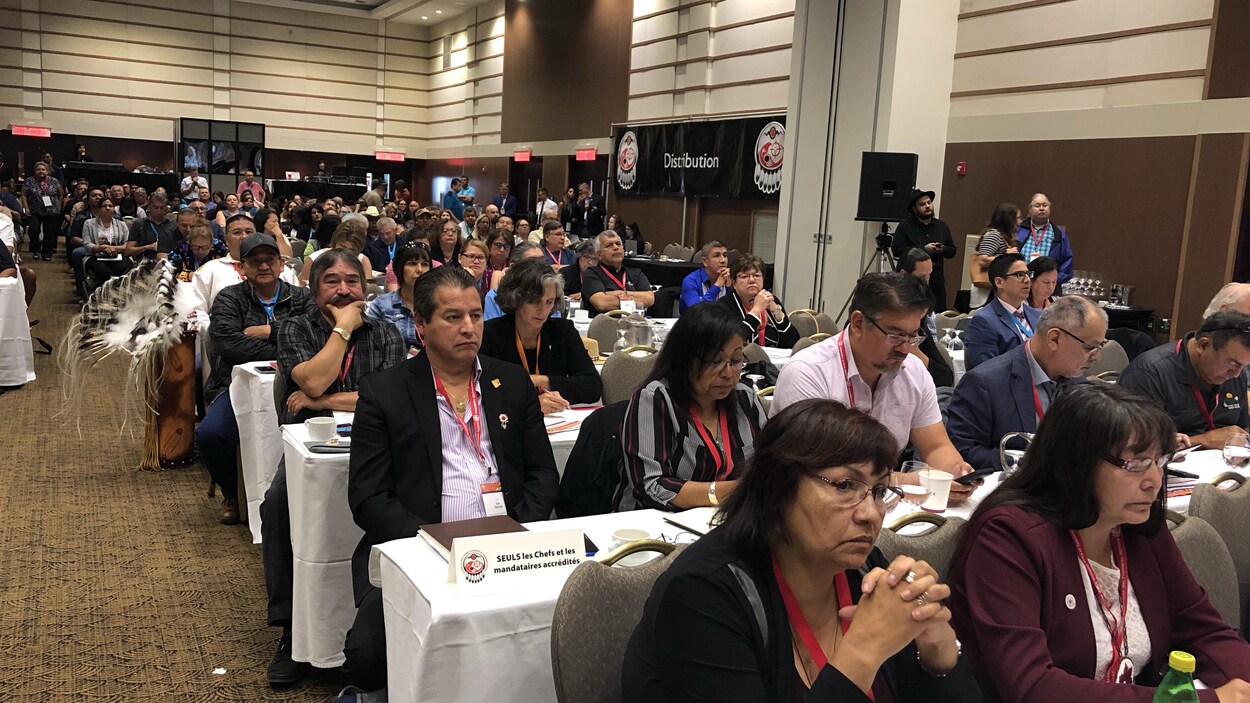 Des personnes assistent à une rencontre dans une grande salle de conférence.