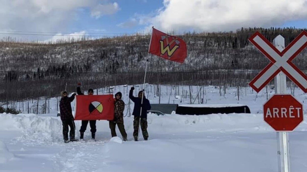 Quatre hommes tiennent des drapeaux tout près d'un passage à niveau.