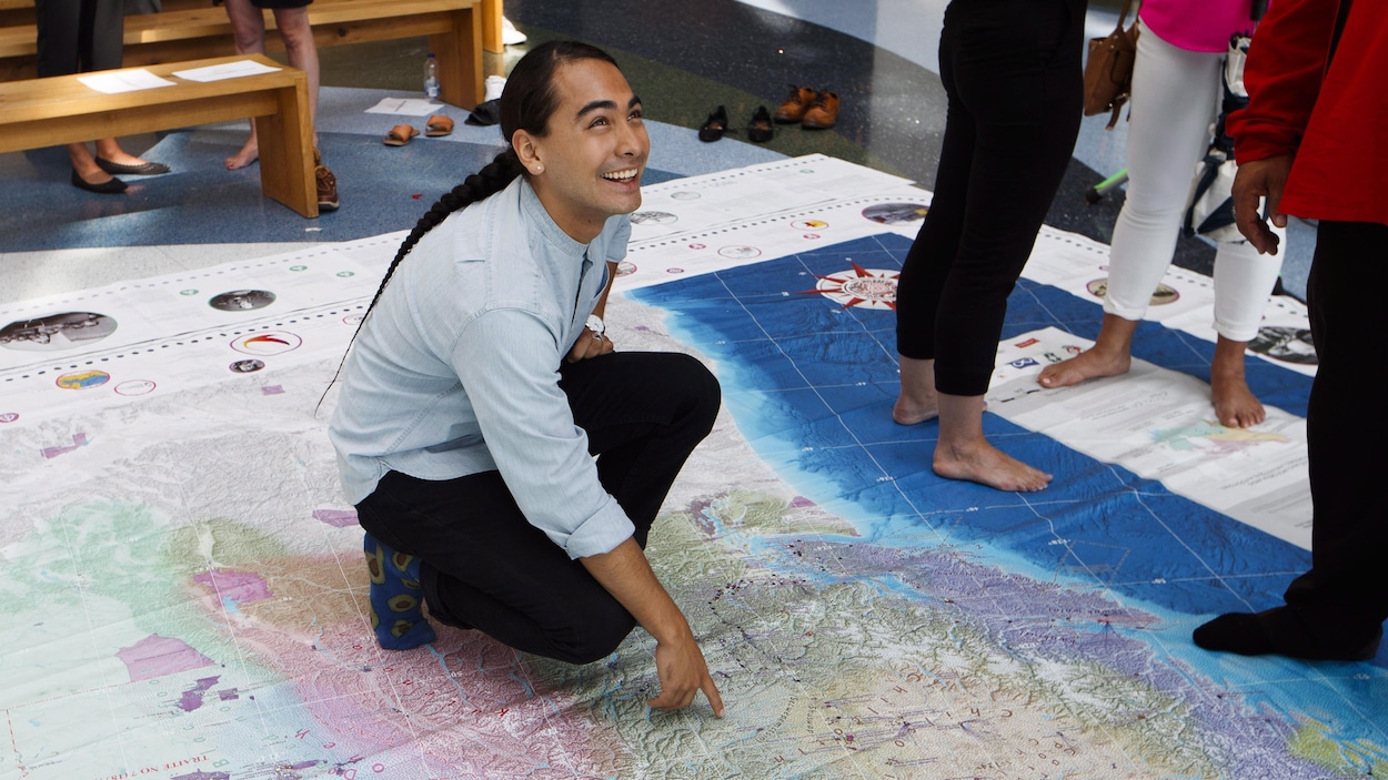 Julian Brave NoiseCat, souriant, montre un endroit sur la carte.