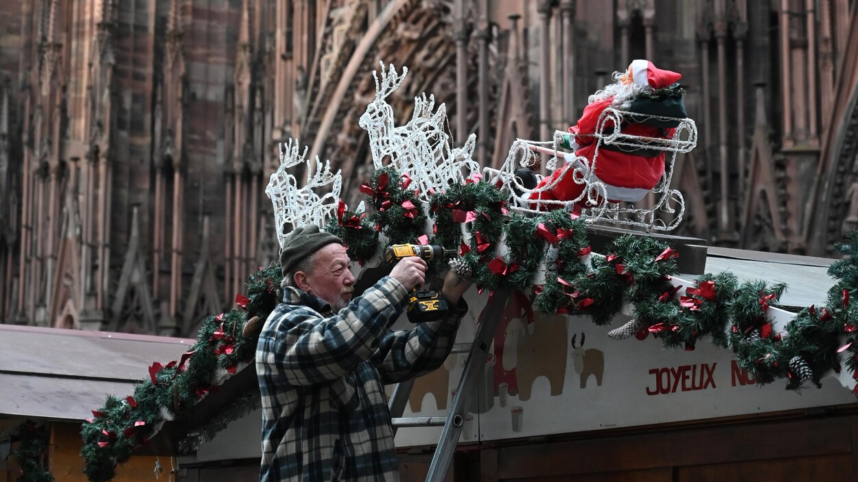 Un vieil homme installe des décorations de Noël au-dessus d'une échoppe.