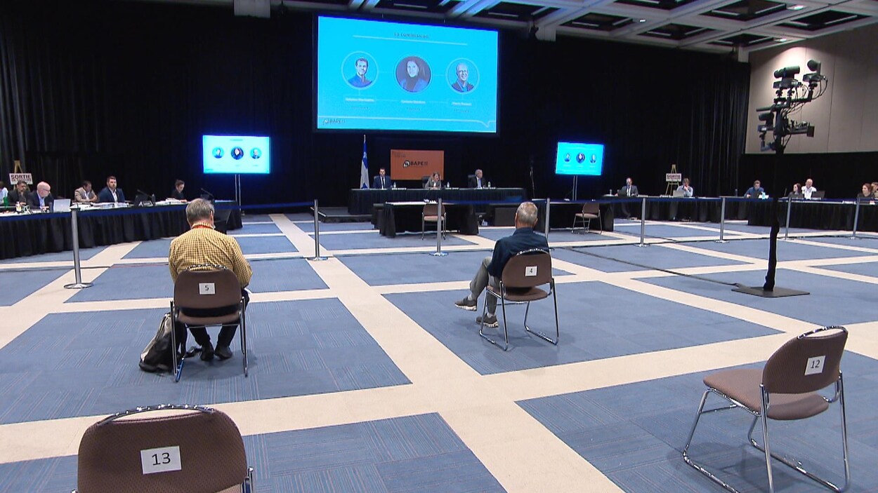 Des personnes assises dans une grande salle participent à des audiences publiques du BAPE.
