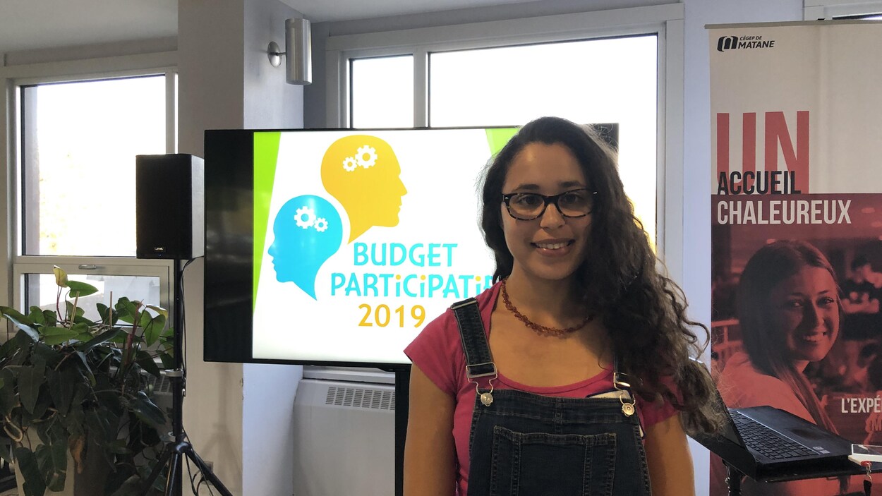 Une jeune femme avec en arrière plan un écran qui présente le logo budget participatif 2019.