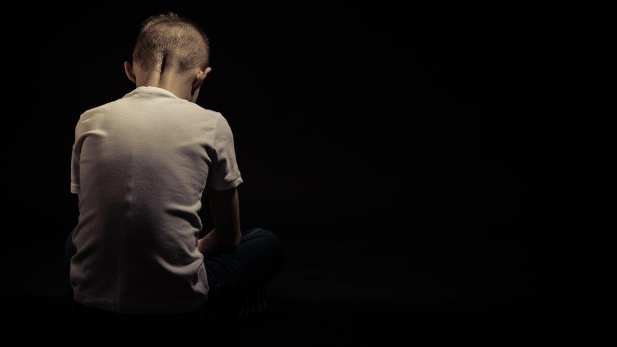 Dans un pièce noire, un enfant autiste de dos la tête baissée. Dans un pièce noire, un enfant autiste de dos la tête baissée.