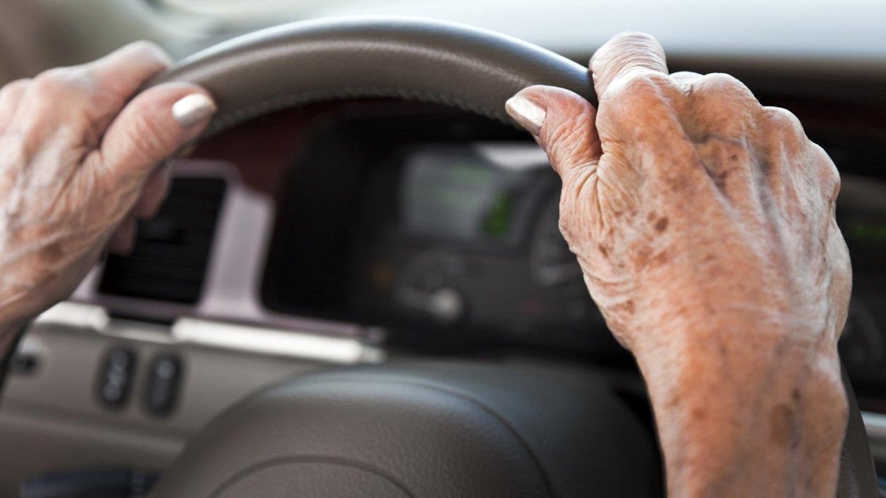 Deux mains d'une femme âgée sont posées sur le volant d'une voiture.
