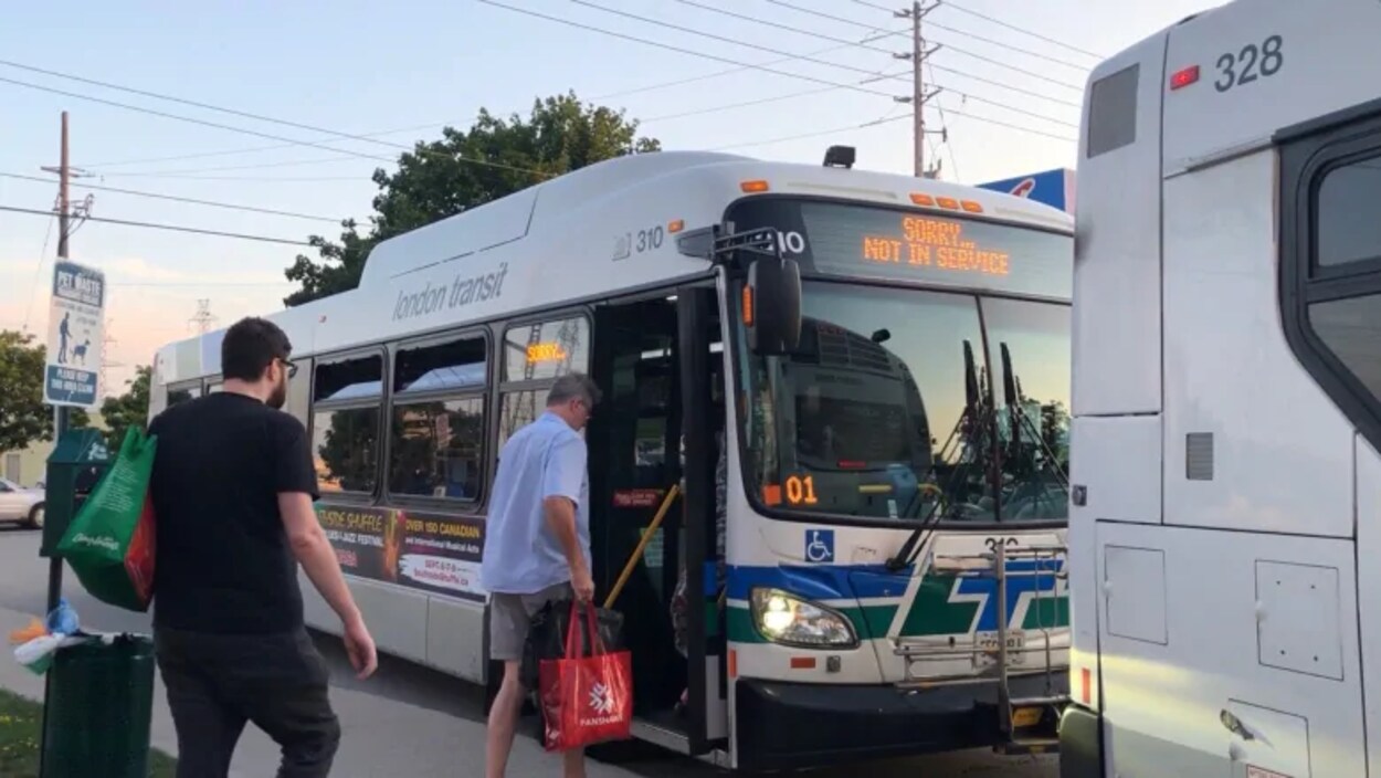 Photo de deux hommes qui montent à bord d'un autobus municipal blanc.