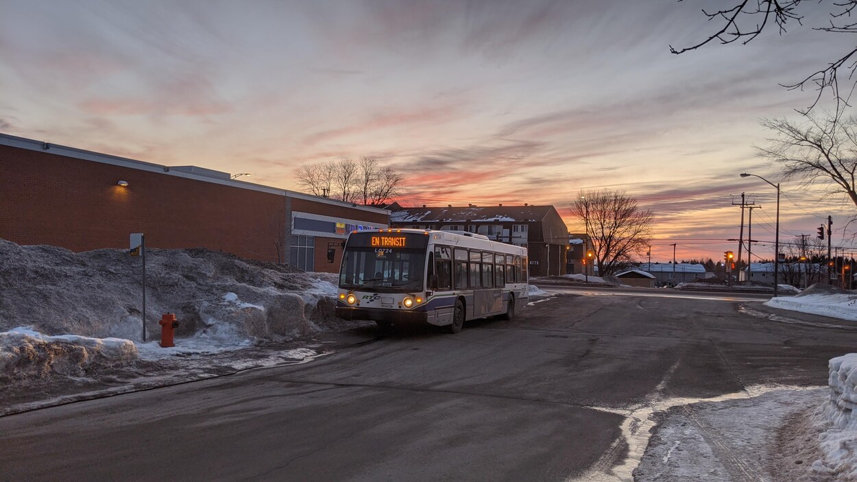 Un autobus en transit stationné près d'une pharmacie. C'est l'hiver, tôt le matin.