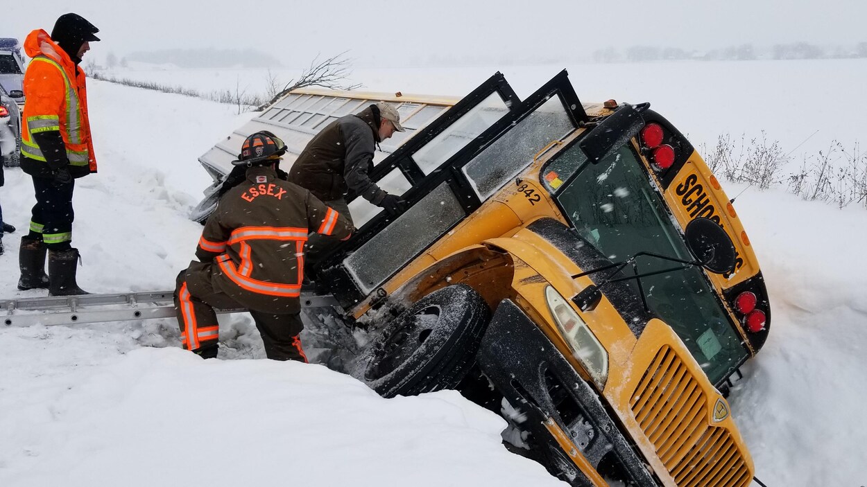 Des pompiers viennent au secours des enfants qui se trouvent dans un autobus jaune, alors que le véhicule est complètement renversé sur son côté dans un fossé enneigé. Des pompiers viennent au secours des enfants qui se trouvent dans un autobus jaune, alors que le véhicule est complètement renversé sur son côté dans un fossé enneigé.