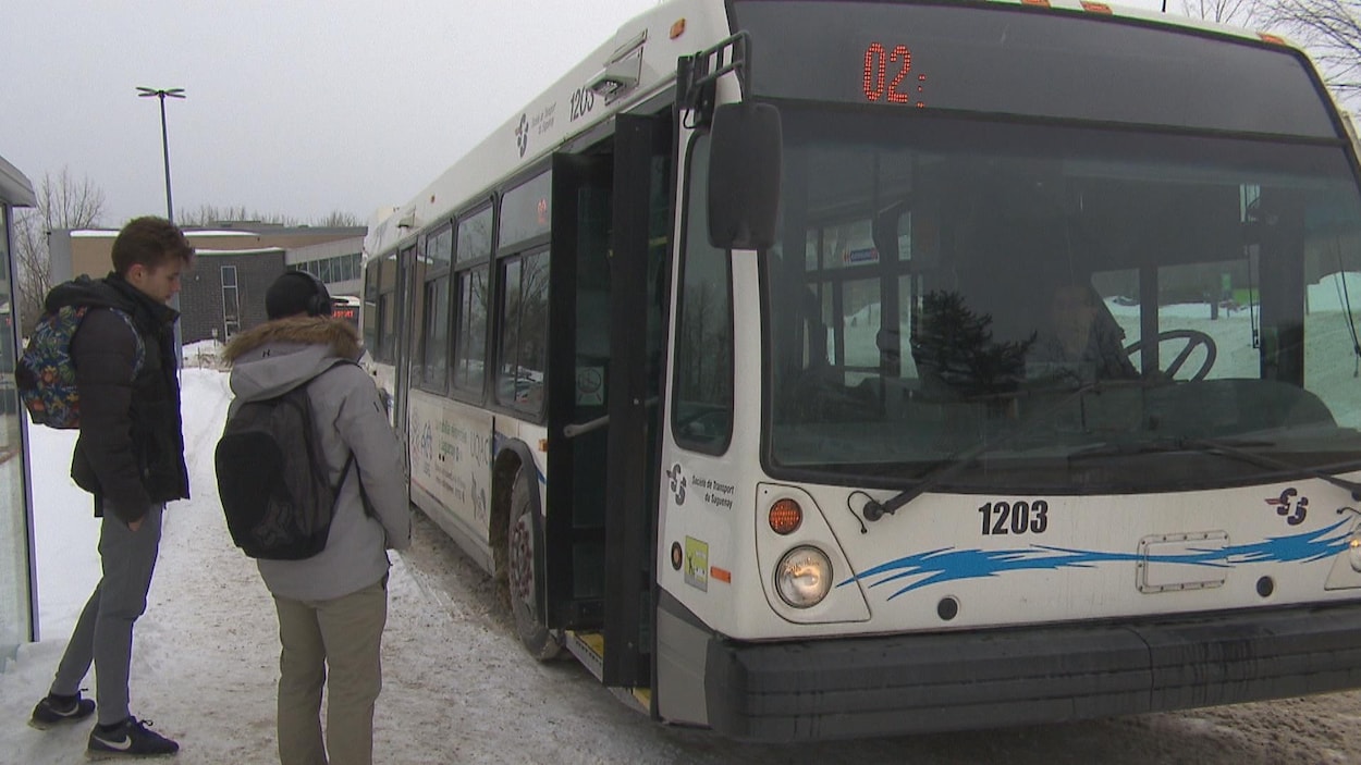Un autobus de la STS avec deux étudiants qui attendent pour embarquer à l'intérieur.