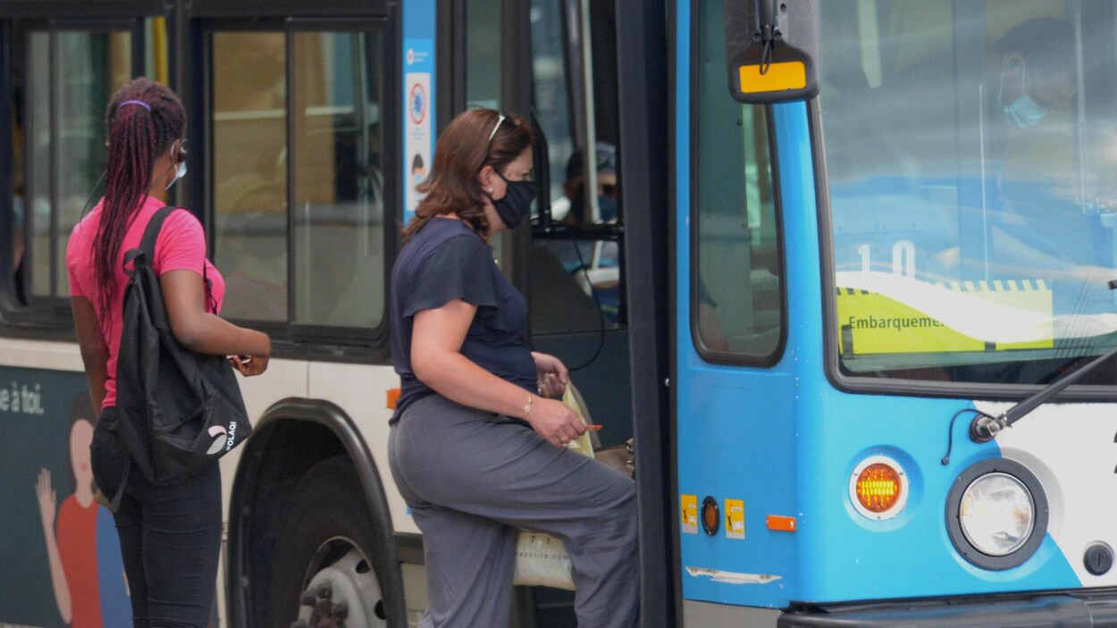 Des usagers avec masque attendent d'entrer dans un autobus.