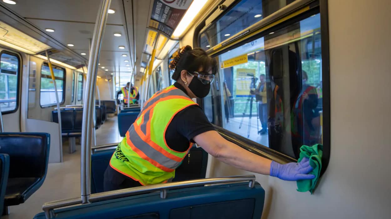 Une femme portant un masque et des gants nettoie une vitre dans une rame de métro.
