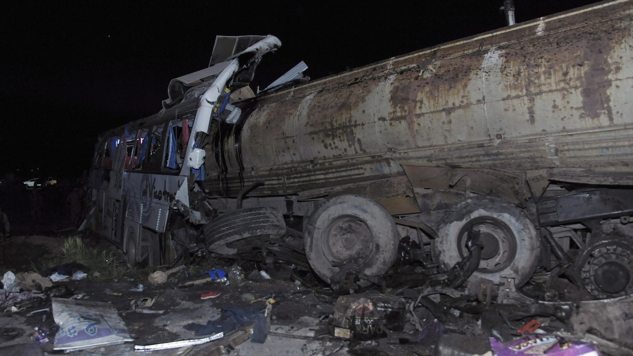 Un camion-citerne et un autobus défoncé entourés de débris.