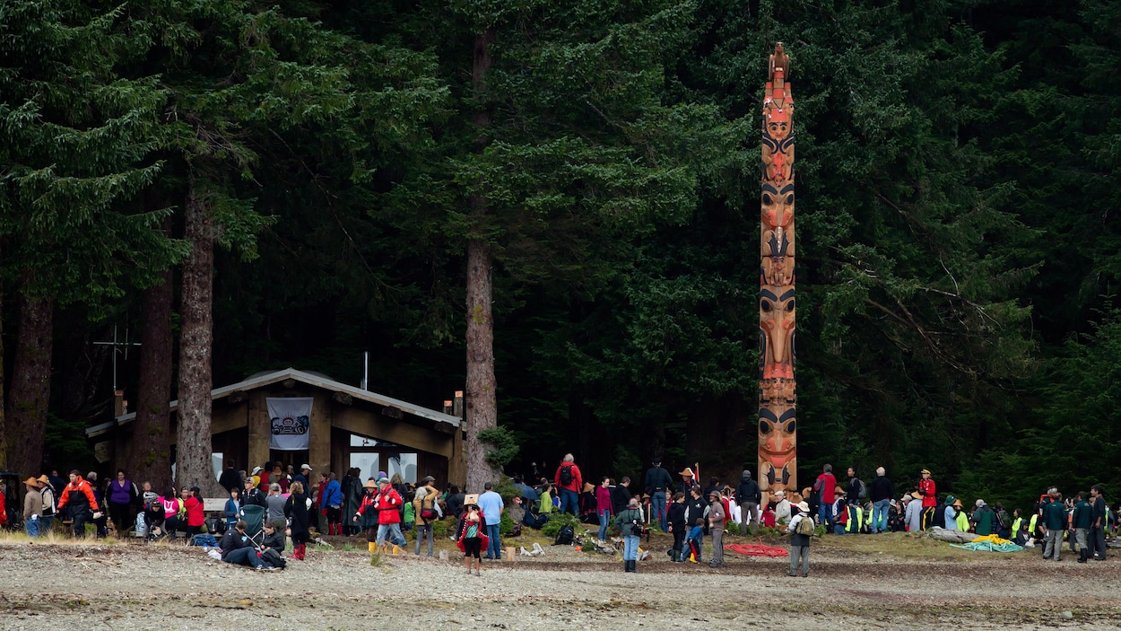 Des touristes au pied d'un totem dans l'archipel d'Haida Gwaii.