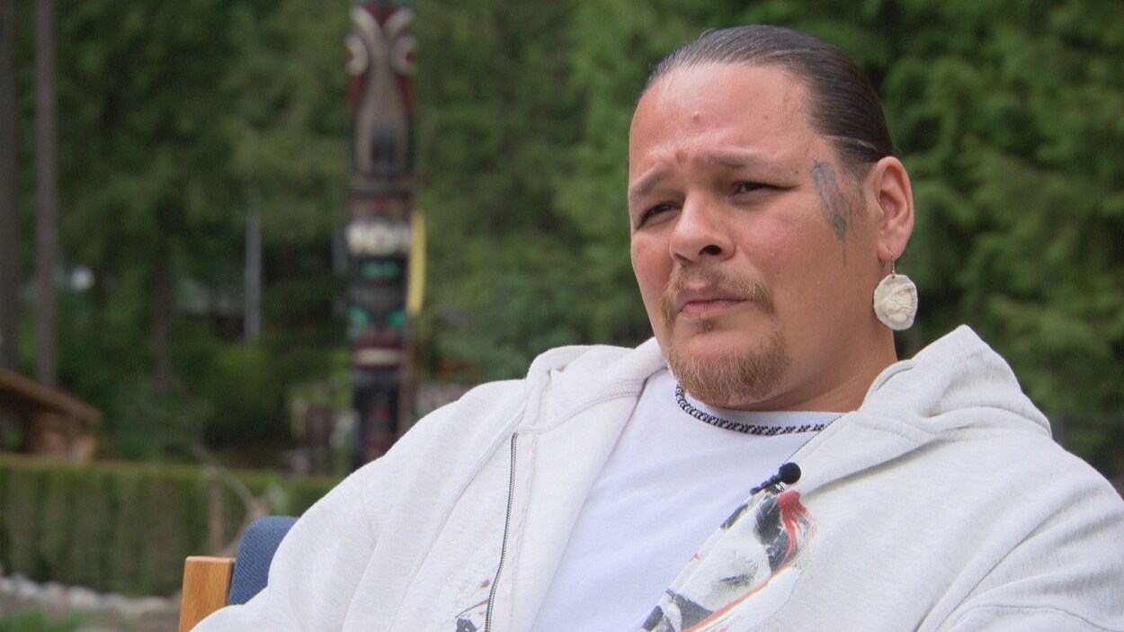 Un homme avec le tatouage d'une plume sur la joue gauche et des boucles d'oreilles regarde au loin. Un homme avec le tatouage d'une plume sur la joue gauche et des boucles d'oreilles regarde au loin.