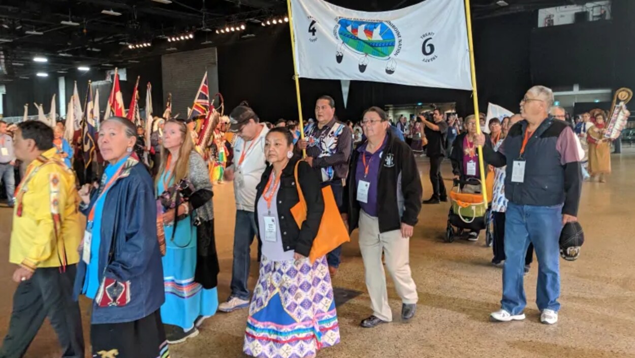 Des aînés autochtones défilent lors d'un rassemblement, des drapeaux et des banderoles à la main.