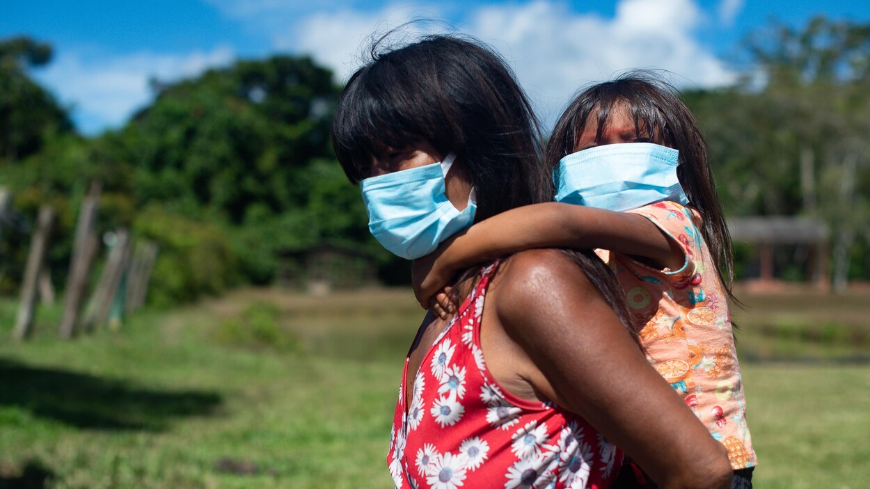 Une mère autochtone porte son enfant sur le dos. Elles portent toutes les deux un masque chirurgical.
