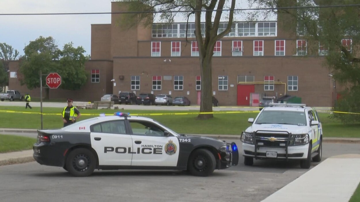 Deux autopatrouilles et des policiers devant une école.