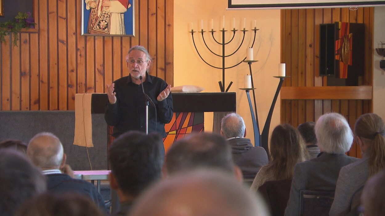 L'historien René Beaudoin est à un micro et parle devant une dizaine de personnes dans une église.