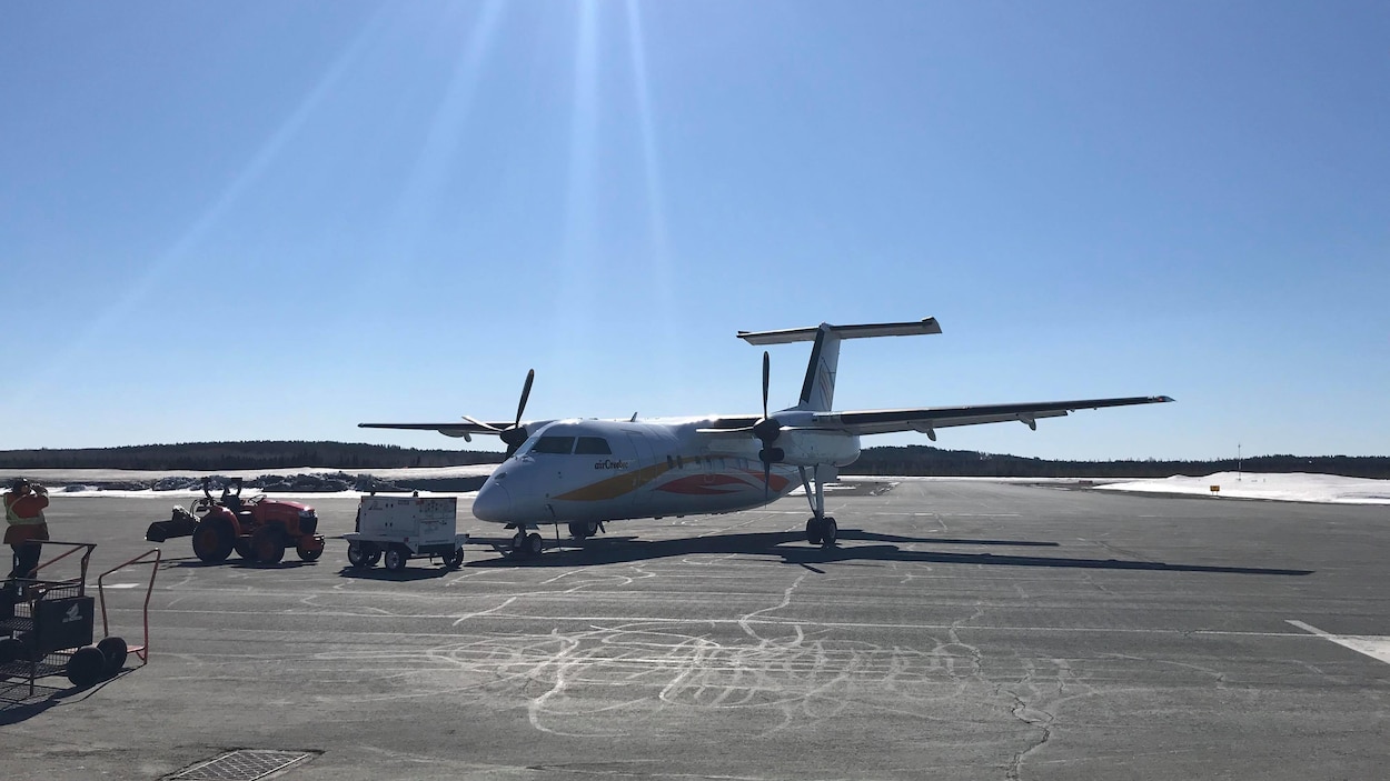 Un avion d'Air Creebec est immobile, un employé de l'aéroport observe l'appareil.