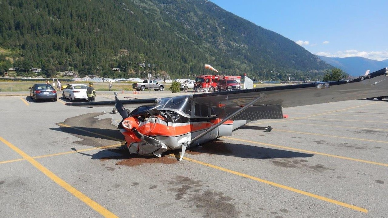 Le petit avion à hélice se trouve au milieu d'un stationnement avec une montagne au loin.