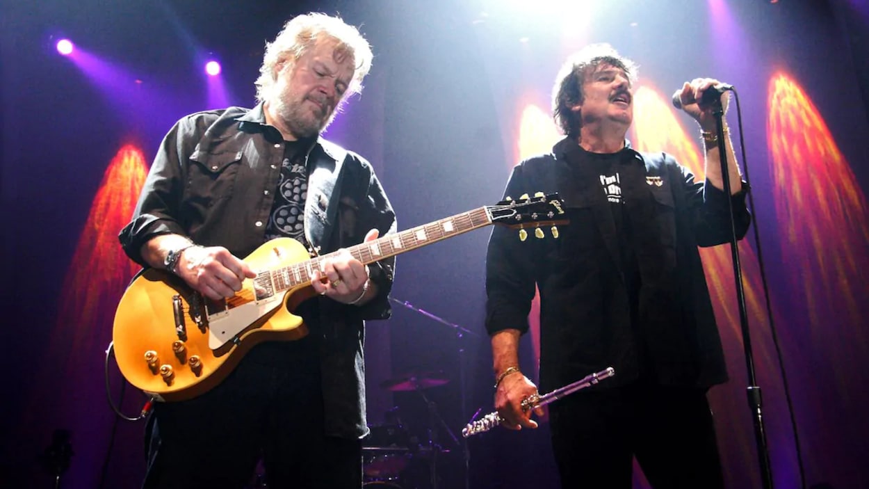 Burton Cummings chantant avec une flûte à la main et Randy Bachman à ses côtés sur scène avec une guitare.