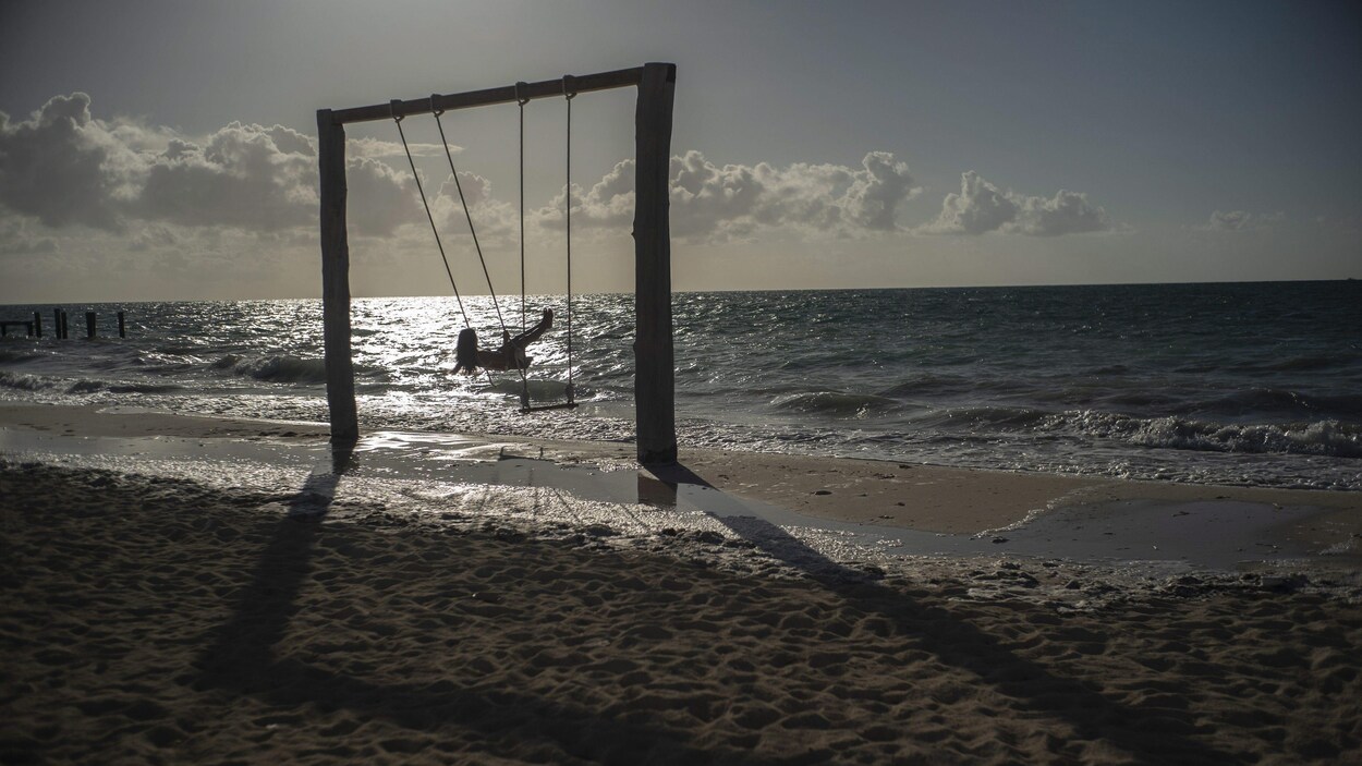 Une femme est dans une balançoire face à la mer.