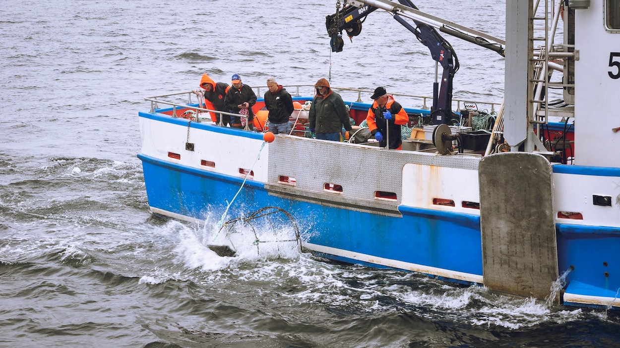 Un bateau avec des hommes qui regardent un engin de pêche qui tombe à l'eau.