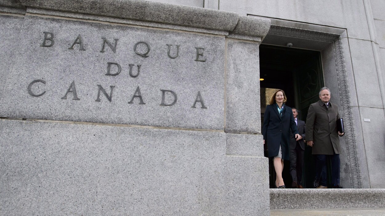 Stephen Poloz, gouverneur de la Banque du Canada et Carolyn Wilkins, première sous-gouverneure, sortent en souriant d'un immeuble sur lequel il est inscrit « Banque du Canada ».