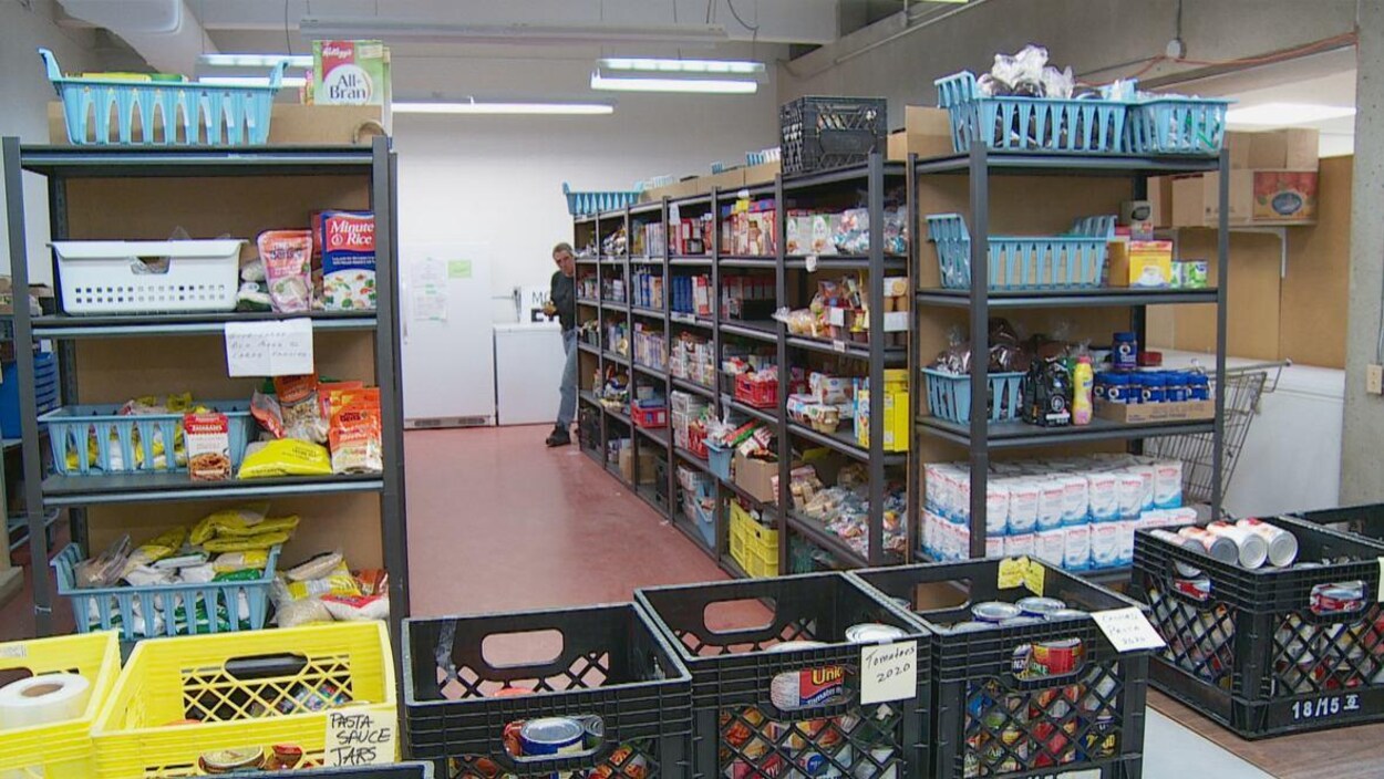 Des étagères remplies de denrées non périssables avec, à l'avant-plan, des paniers contenant des conserves posés sur une table.