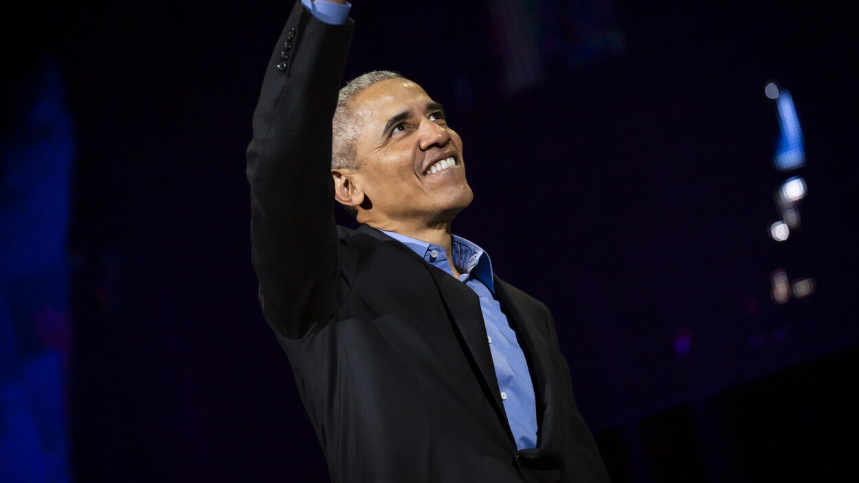 Barack Obama salue la foule, un bras dans les airs et un grand sourire aux lèvres.