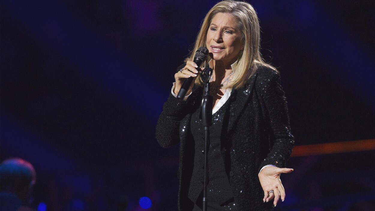 Barbra a un micro à la main et chante sur la scène. Barbra a un micro à la main et chante sur la scène.
