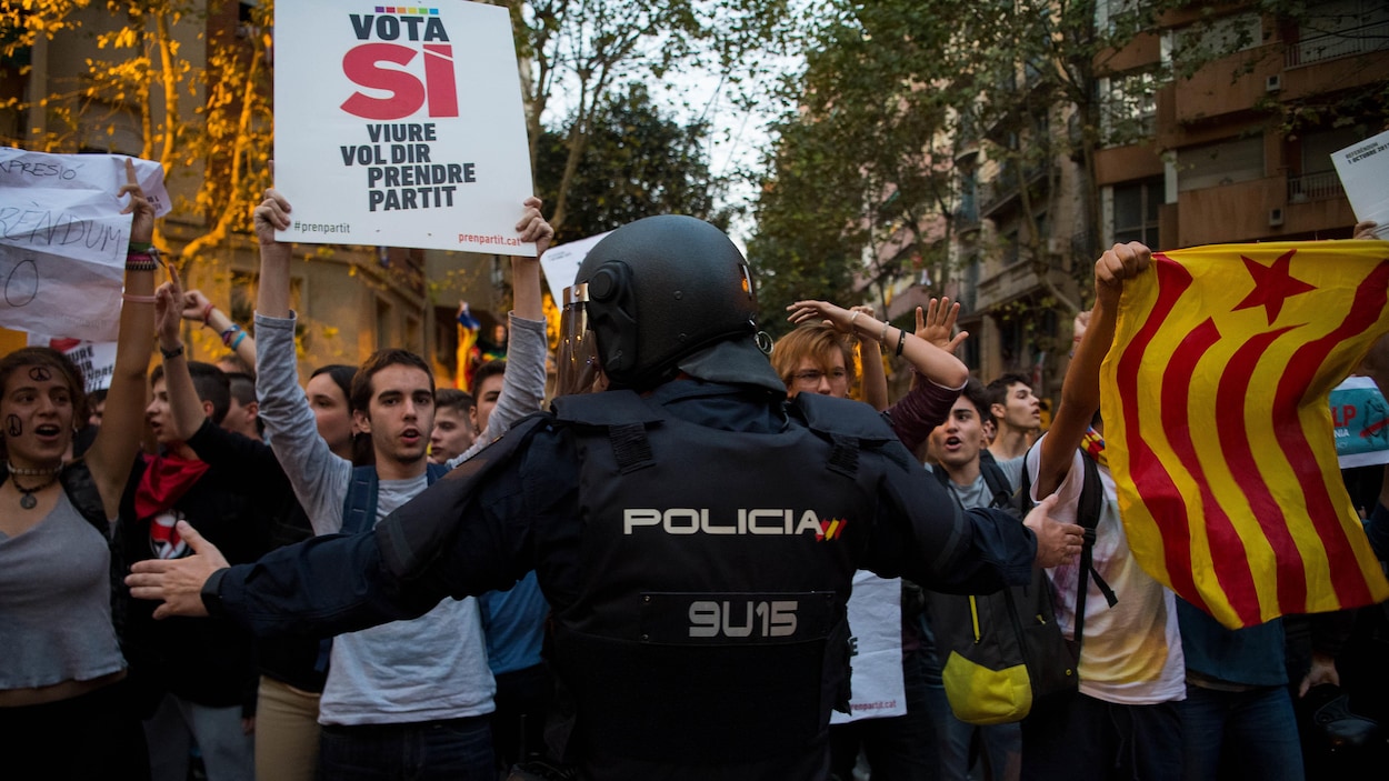 Une foule de Catalans manifeste devant un policier qui leur bloque la voie.