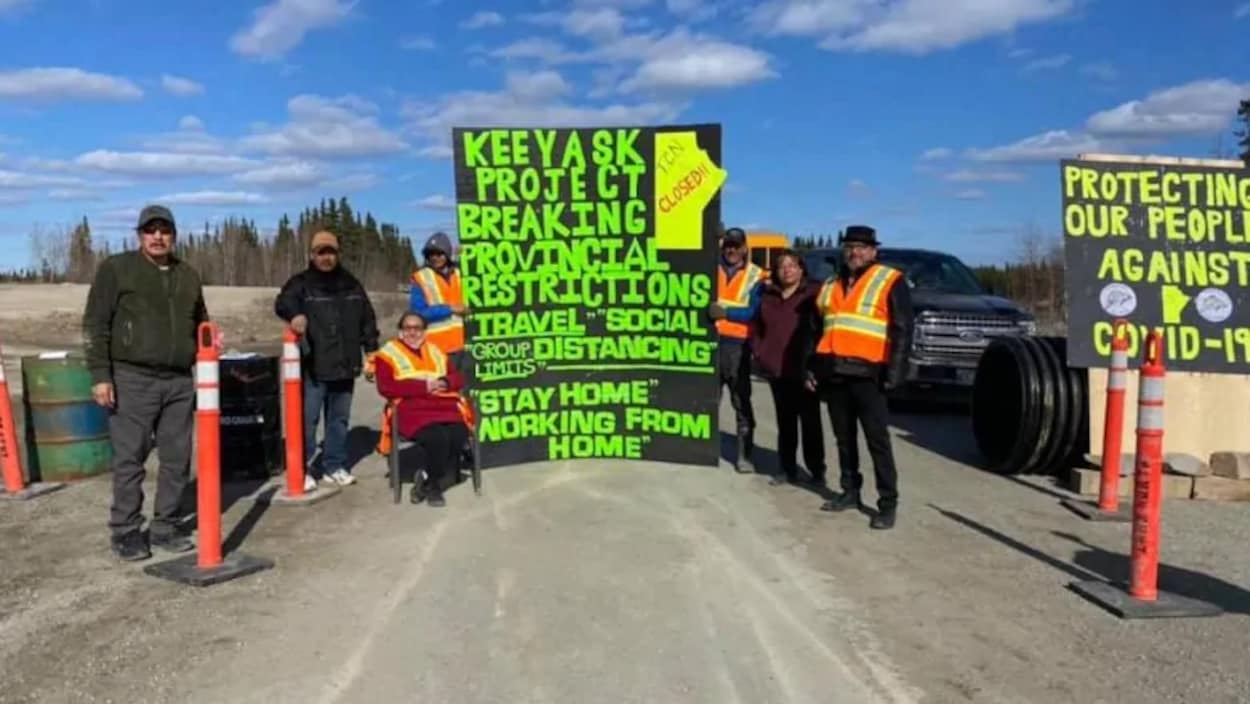 Des hommes et des femmes autochtones bloquant une autoroute avec des pancartes expliquant qu'ils tentent de protéger les leurs de la pandémie.
