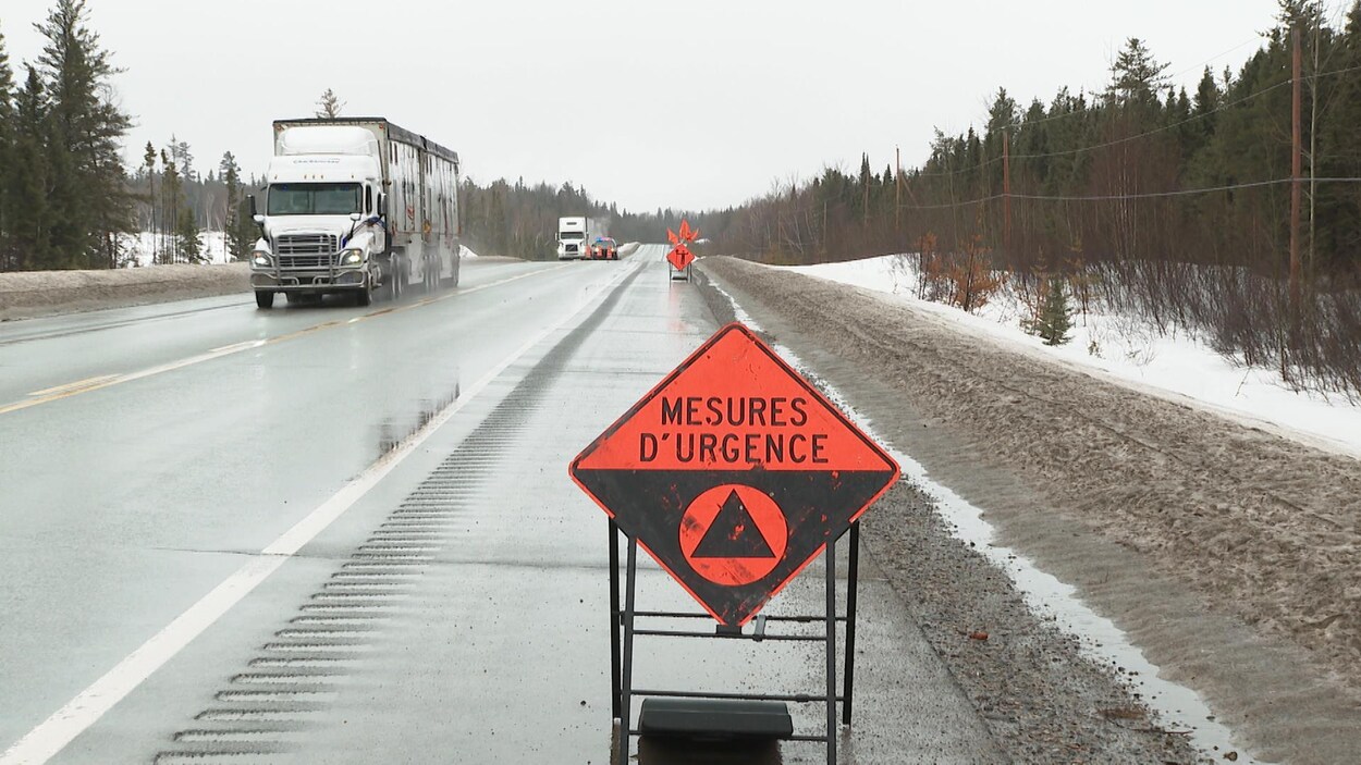 Une pancarte où il est indiqué Mesures d'urgence en bordure de la route. Au loin, un véhicule de la Sûreté du Québec est stationné au milieu de la route.
