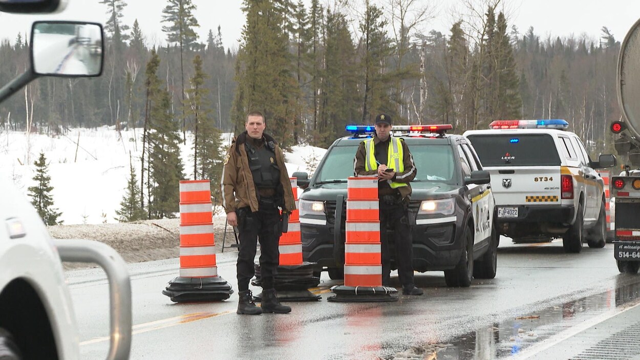 Deux policiers se tiennent debout devant leur véhicule et attendent qu'un camion s'arrête à côté d'eux.