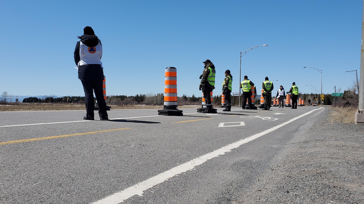 Des policiers en dossards jaunes fluo sont l'un en arrière de l'autre vis-à-vis des cônes, debout sur la route.